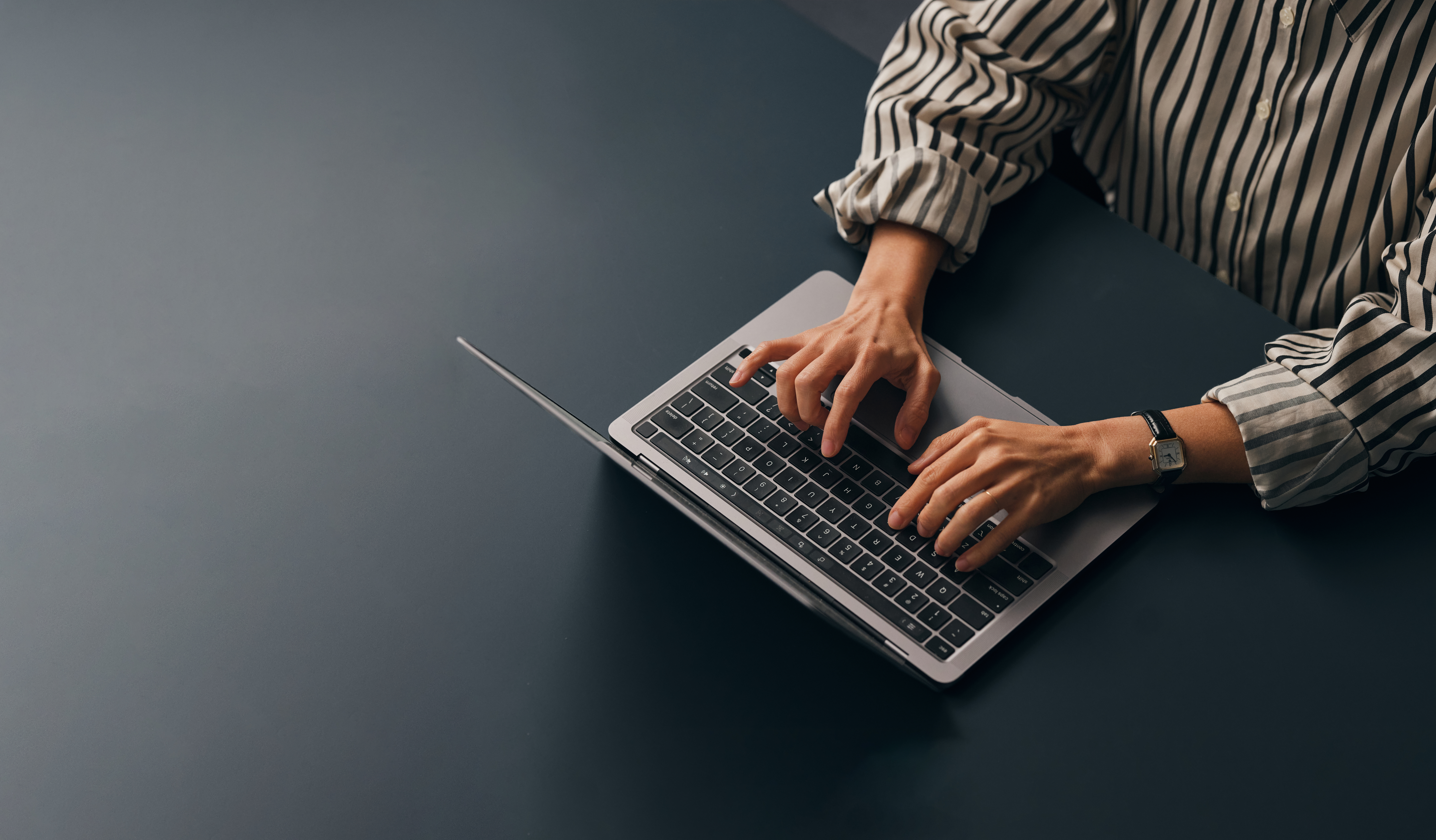 A from above view of an unrecognizable Caucasian copywriter typing on her laptop while sitting at her office desk. (copy space)